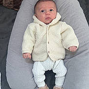 Elyo participe au concours pour gagner de l'argent avec cette photo : baby, cartoon, child, comfortable, curious, cushion, cute, face, gray, indoor, infant, knitted_clothing, person, plush, sitting, slippers, soft, toy, warm_clothing, white_clothing