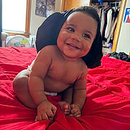 Atlantic is registered to the contest to win money with this photo: baby, smiling, red_bedspread, indoor, child, happy, clothing, blanket, bed, room, window, closet, furniture, portrait, infant, hand, foot, skin, face, expression