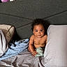 baby, child, bed, pillow, blanket, soft_toy, curly_hair, indoor, portrait, infant, cute, skin, expression, looking_at_camera, holding, cloth, headboard, resting, comfort, young