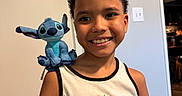 Seth joined the competition — help win amazing prizes! child, boy, smile, plush_toy, stitch, indoor, tank_top, curly_hair, shoulder, happy, portrait, room, wall, doorway, light_switch, wood_floor, casual, toy, person, home