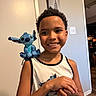 boy, casual, child, curly_hair, doorway, happy, home, indoor, light_switch, person, plush_toy, portrait, room, shoulder, smile, stitch, tank_top, toy, wall, wood_floor