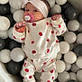 Lyna a rejoint le concours — aidez-le/la à gagner de superbes lots ! baby, ball_pit, balls, child, clothing_pattern, comfort, cute, face, footwear, hands, headband, indoor, infant, lying_down, pacifier, play_area, red_apples, shoes, soft_toys, white_clothing