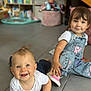 baby, toddler, child, floor, denim_overalls, white_shirt, pink_shoes, smiling, indoor, playroom, toy, bookshelf, tile_floor, person, happy, cute, candid, young_child, casual_clothing, home