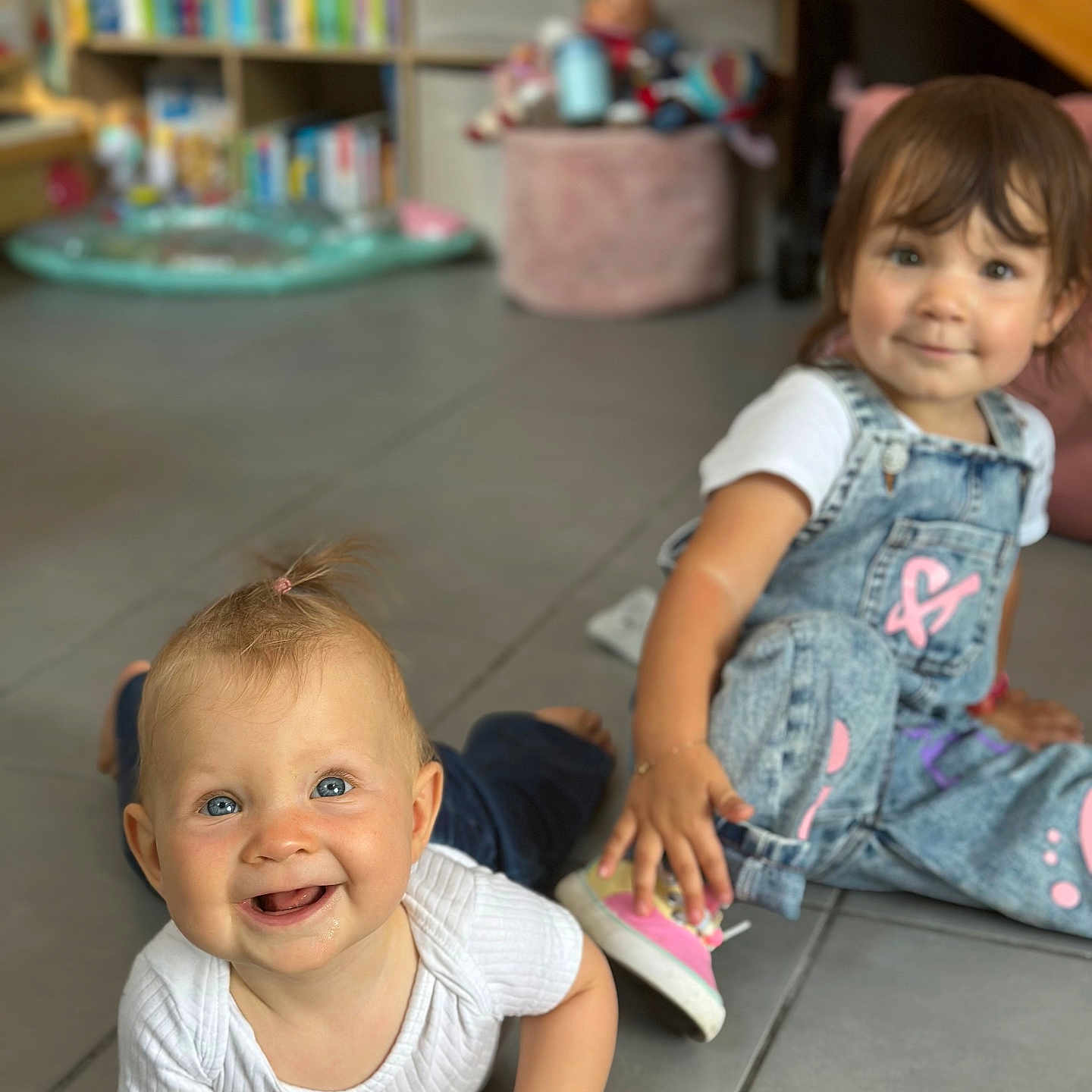 Henrya participe au concours pour gagner de l'argent avec cette photo : baby, bookshelf, candid, casual_clothing, child, cute, denim_overalls, floor, happy, home, indoor, person, pink_shoes, playroom, smiling, tile_floor, toddler, toy, white_shirt, young_child