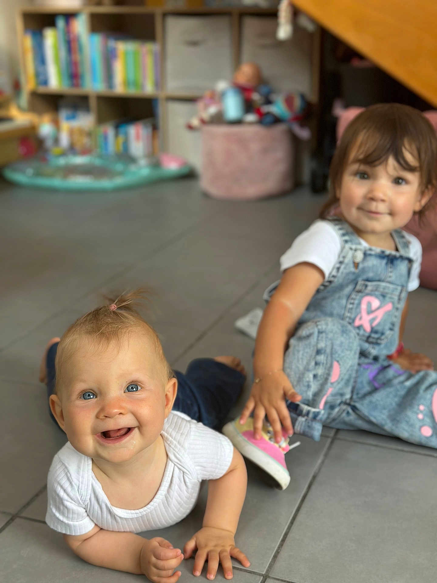 Henrya participe au concours pour gagner de l'argent avec cette photo : baby, toddler, child, floor, denim_overalls, white_shirt, pink_shoes, smiling, indoor, playroom, toy, bookshelf, tile_floor, person, happy, cute, candid, young_child, casual_clothing, home