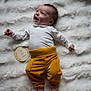 2_months, baby, bare_feet, child, cozy, cute, fluffy_blanket, happy, indoors, infant, lying_down, milestone, newborn, portrait, small_hands, smiling, soft_texture, white_onesie, wooden_plaque, yellow_pants