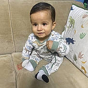 Roberto Paramo is registered to the contest to win money with this photo: toddler, child, pajamas, dinosaur_print, couch, beige, pillow, dinosaur, socks, mismatched_socks, indoor, smiling, sitting, cute, curious, clothing, baby, furniture, portrait, young_child