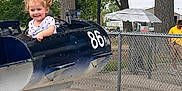 Brooklynn joined the competition — help win amazing prizes! child, girl, amusement_ride, airplane, outdoor, playground, smiling, happy, pigtails, curly_hair, fence, trees, concrete, casual_clothing, park, person, daytime, fun, ride, vehicle