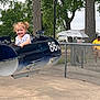 child, girl, amusement_ride, airplane, outdoor, playground, smiling, happy, pigtails, curly_hair, fence, trees, concrete, casual_clothing, park, person, daytime, fun, ride, vehicle