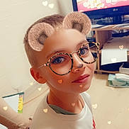 Noam participe au concours pour gagner de l'argent avec cette photo : child, boy, face_filter, glasses, bear_ears, hearts_overlay, television, cartoon, living_room, sitting, sweater, short_hair, smiling, portrait, indoor, wooden_floor, shelf, box, tissue_box, playful
