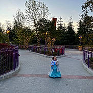 Gabriella participe au concours pour gagner de l'argent avec cette photo : child, girl, princess_dress, toy, stuffed_animal, park, trees, lights, pathway, purple_railings, evening, outdoor, nature, pavement, lanterns, costume, young_child, playful, twilight, scenic