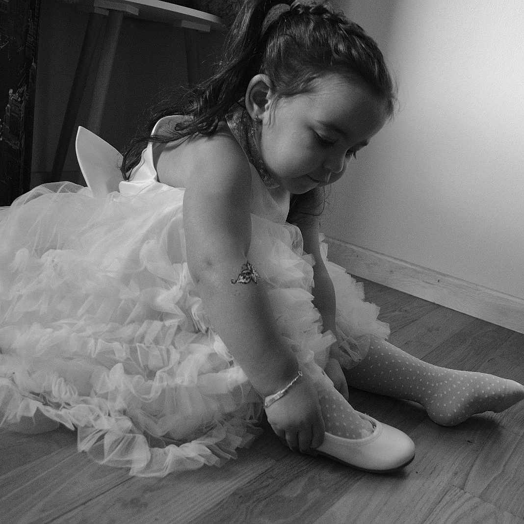 Gabriella participe au concours pour gagner de l'argent avec cette photo : child, girl, dress, shoe, sock, floor, indoor, black_and_white, portrait, concentration, sitting, wooden_floor, furniture, hair, cute, toddler, bracelet, tattoo, wall, light