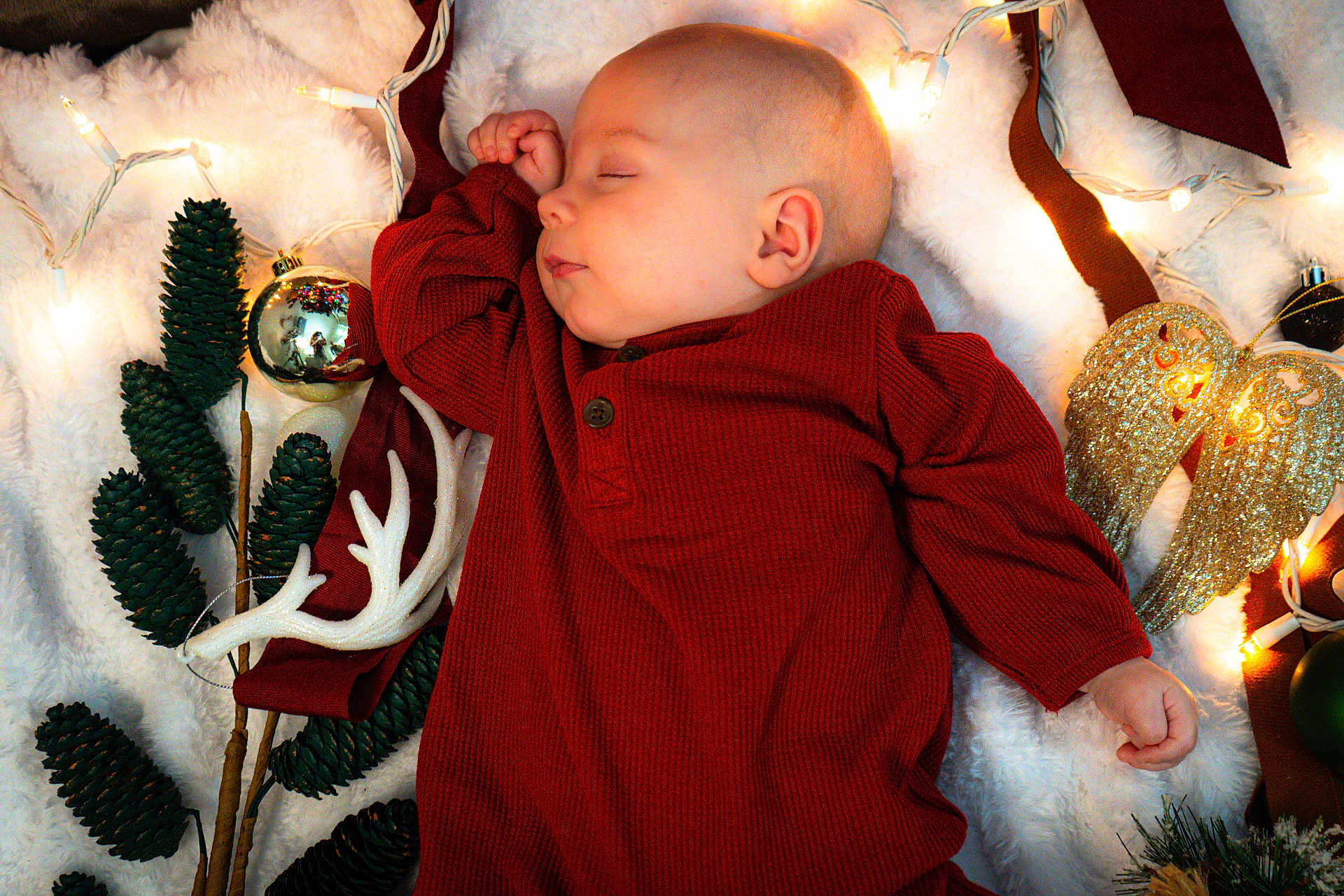 Jack is registered to the contest to win money with this photo: baby, sleeping, red_clothing, blanket, pinecones, christmas_lights, ornaments, angel_wings, holiday, festive, decoration, cozy, infant, cute, peaceful, indoor, portrait, holiday_theme, soft_texture, warm_colors