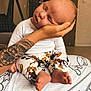 baby, infant, sleeping, hand, tattoo, pants, cartoon_print, blanket, indoor, lamp, foot, person, head, cozy, bedroom, rest, comfort, soft, cute, peaceful