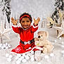 celebration, child, christmas, cozy, cute, festive, happy, headband, holiday_decor, indoor, lantern, red_dress, sitting, smiling, snow_balls, teddy_bear, toddler, toy, white_star, winter_scene