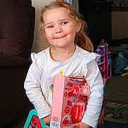 Taelynn is registered to the contest to win money with this photo: child, toddler, smiling, toy, toy_box, tea_set, toy_cart, doll_house, living_room, couch, sofa, white_shirt, long_sleeves, ponytail, hair, carpet, hands, indoor, candid, happy