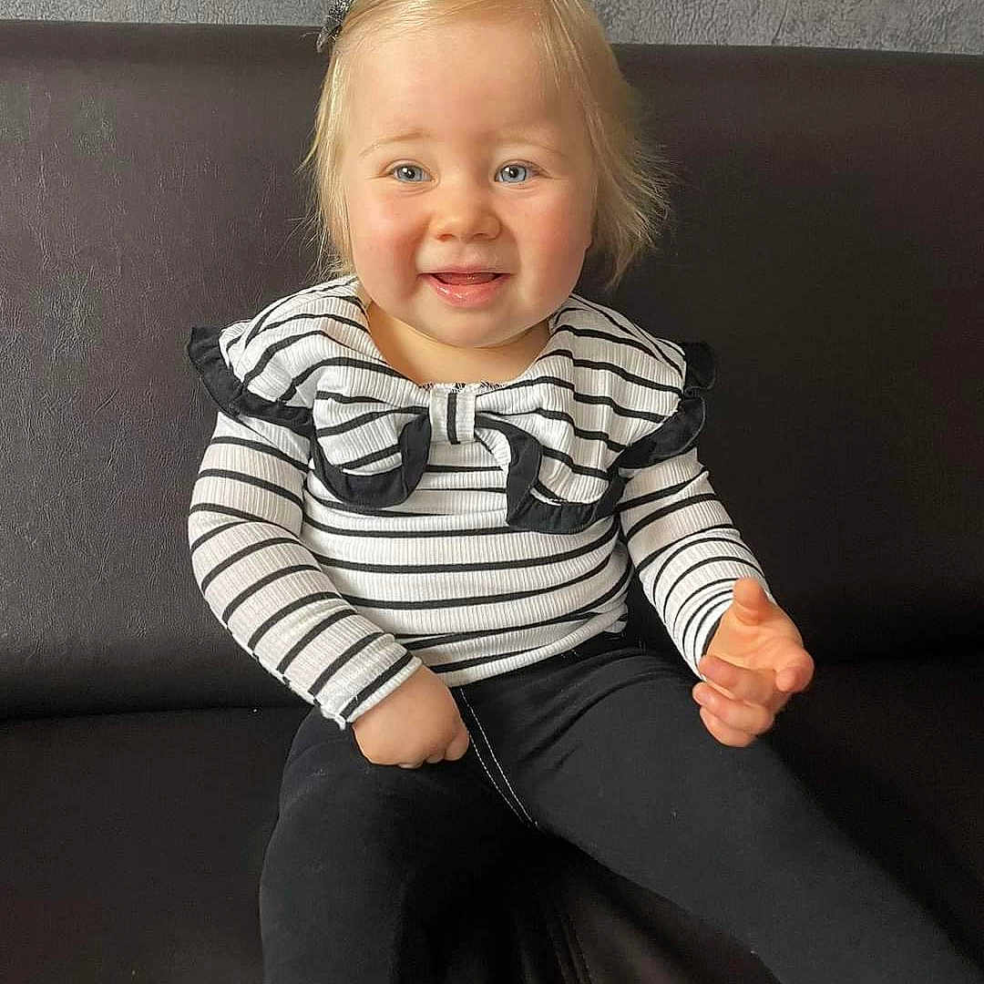 Mya participe au concours pour gagner de l'argent avec cette photo : baby, babylaughing, blonde, clothing, couch, face, furniture, hair, happy, head, jeans, knitwear, pants, person, photography, portrait, sitting, sleeve, smile, sweater