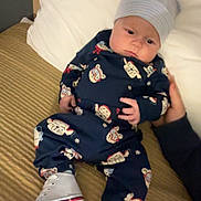 Warren is registered to the contest to win money with this photo: baby, infant, bed, blanket, hat, onesie, footwear, sneakers, hand, person, face, cute, sleepwear, child, lying_down, indoors, expression, soft_lighting, comfort, resting