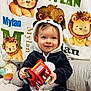 baby, child, toy_truck, panda_onesie, blanket, lion_illustration, stuffed_toy, cushion, smile, indoor, cute, happy, playful, clothing, person, portrait, infant, soft_toy, colorful, seated