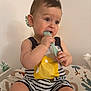 Mylan participe au concours pour gagner de l'argent avec cette photo : baby, child, comb, chewing, striped_clothing, yellow_fish, sitting, cushion, patterned, indoor, curious, cute, infant, romper, hand, face, wall_decor, room, toy, skin