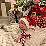 Isaï participe au concours pour gagner de l'argent avec cette photo : baby, santa_hat, candy_cane, blanket, christmas_tree, ornaments, presents, holiday, festive, floor, tiled_floor, toy, red, white, green, face, cute, infant, indoors, decorations