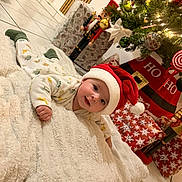 Isaï participe au concours pour gagner de l'argent avec cette photo : baby, santa_hat, blanket, christmas_tree, ornaments, lights, presents, nutcracker, floor_tiles, holiday, festive, indoors, cute, smiling, child, winter_clothing, decorations, red, green, white