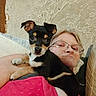 Cozmo is registered to the contest to win money with this photo: animal, black, brown, casual, closeup, cute, dog, face, glasses, indoor, person, pet, pink_clothing, puppy, resting, shoulder, tan, texture, wall, young_dog