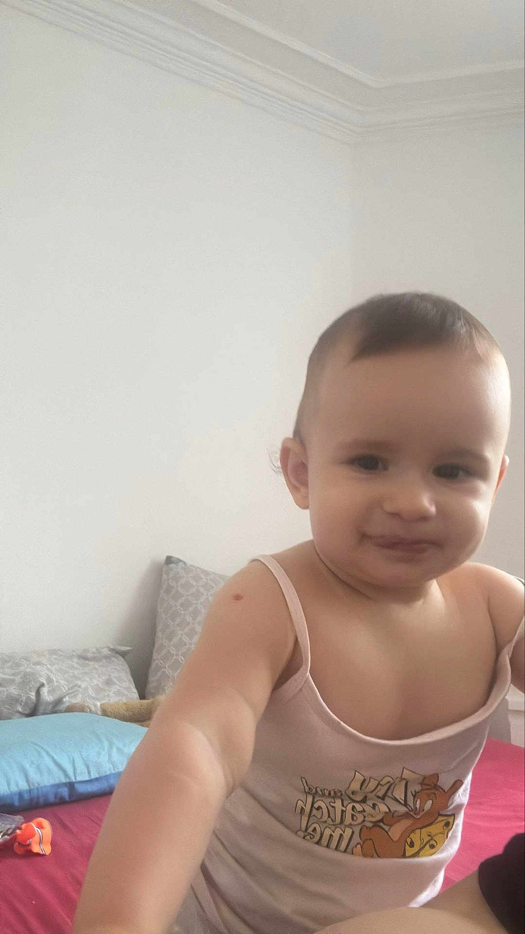 Selvi a rejoint le concours — aidez-le/la à gagner de superbes lots ! toddler, child, bed, pillow, tank_top, indoor, smiling, face, person, cute, clothing, baby, cartoon_character, tom_and_jerry, red_bedspread, white_wall, short_hair, playful, skin, room