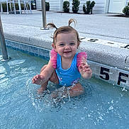 Alina is registered to the contest to win money with this photo: toddler, child, water, swimsuit, splashing, pool, pigtails, smiling, outdoor, summer, fun, play, blue, pink, wet, happy, person, young_child, sitting, recreation