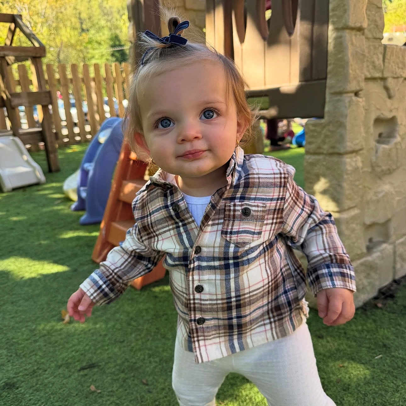 Alina joined the competition — help win amazing prizes! blue_eyes, brown_shoes, casual_clothing, child, curious, cute, daylight, fence, grass, nature, outdoor, person, plaid_shirt, play_structure, playground, sunlight, toddler, topknot, white_leggings, young_child