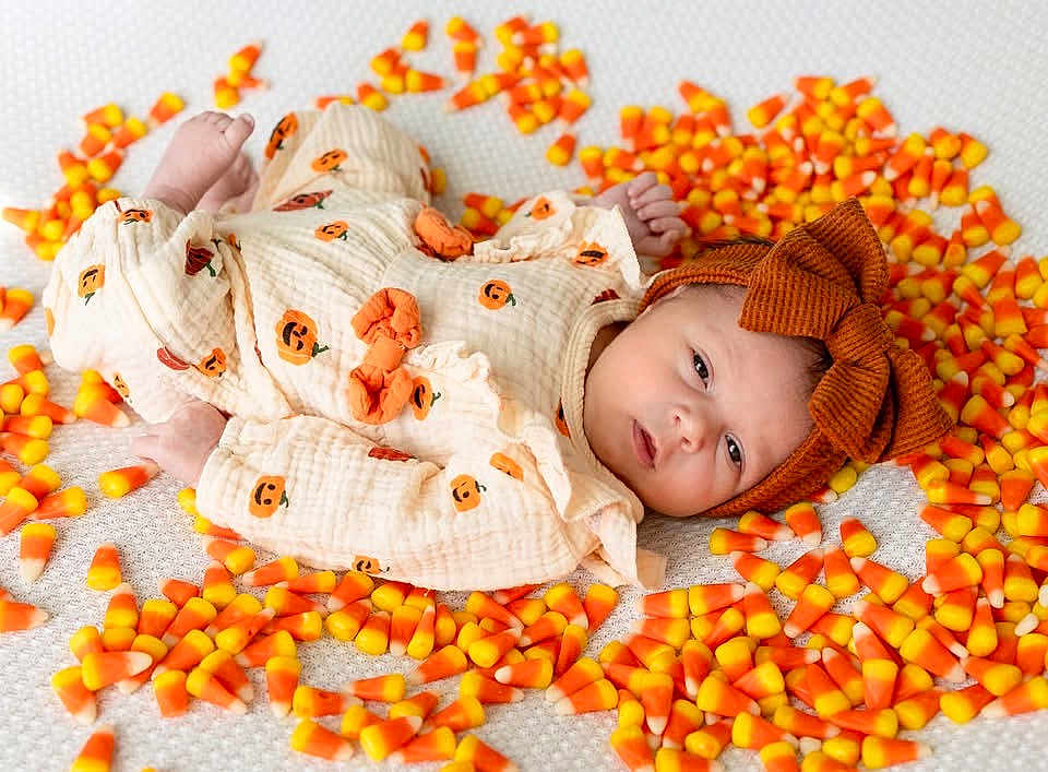 Evelyn is registered to the contest to win money with this photo: baby, infant, candy_corn, pumpkin_outfit, headband, brown_bow, cute, lying_down, white_background, holiday_theme, fall, autumn, soft_texture, baby_clothing, child, portrait, sweet, colorful, festive, holiday