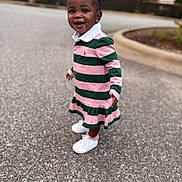 Rumani is registered to the contest to win money with this photo: toddler, child, smiling, outdoor, paved_road, dress, striped_clothing, pink, green, hair_bows, white_sneakers, earrings, happy, standing, person, curb, blurred_background, nature, daylight, fashion