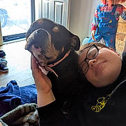Echo is registered to the contest to win money with this photo: affection, black_dog, blanket, creepy_doll, cuddle, dog, doll, door, floor, glasses, hand, head, indoor, natural_light, overalls, person, smile, striped_shirt, table, tan_markings