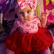 Cierra is registered to the contest to win money with this photo: baby, child, tutu_skirt, headband, bow, pink_clothing, red_skirt, sitting, blanket, pillow, face, expression, indoor, cute, plush, patterned_clothing, person, infant, portrait, curious_eyes