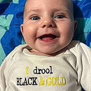 Cierra joined the competition — help win amazing prizes! baby, smiling, infant, face, clothing, blue_blanket, happy, closeup, cute, child, mouth_open, eyes, cheeks, sitting, text_on_clothing, indoors, young_child, person, portrait, fabric