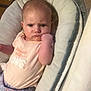 baby, infant, child, serious_expression, clenched_fist, pink_shirt, patterned_pants, baby_seat, cushion, soft_texture, indoor, person, portrait, young_child, cute, closeup, comfortable, lighting, expression, casual_clothing