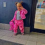 toddler, child, pink_jacket, pink_pants, heart_pattern, backpack, smile, indoor, floor_tiles, door, glass, window, wall, electric_outlet, shoe, person, hair_puffs, playful, gesture, parking_lot