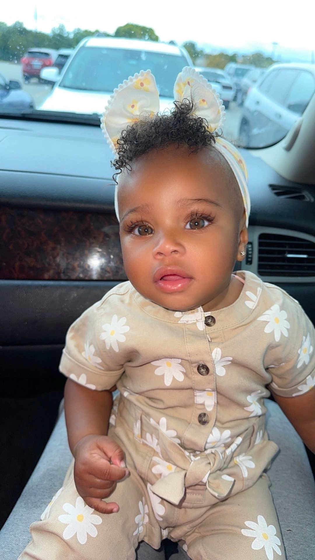 Ahyokaa is registered to the contest to win money with this photo: toddler, child, baby, curly_hair, headband, bunny_ears, beige_outfit, daisy_pattern, car_interior, car_seat, window, parked_cars, cute, portrait, clothing, face, eyes, hand, expression, indoor