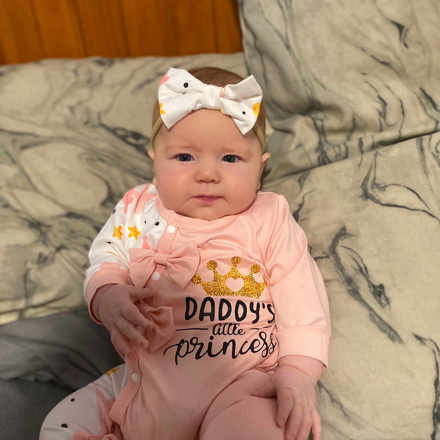 Aeva is registered to the contest to win money with this photo: baby, bow, child, chubby_cheeks, crown, cushion, cute, expression, face, hand, headband, indoor, infant, marble_pattern, onesie, pink_clothing, portrait, sitting, text_on_clothing, young_child