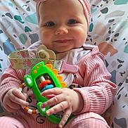 Grace is registered to the contest to win money with this photo: baby, bow, child, closeup, cushion, cute, face, green_toy, hand, happy, headband, indoors, infant, patterned_cushion, person, pink_clothing, playful, sitting, smiling, toy