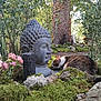 cat, buddha_statue, garden, moss, tree_trunk, rocks, flowers, greenery, outdoor, nature, sunlight, peaceful, curious_cat, statue, plant, shrub, serene, daylight, calm, closeup