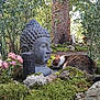 cat, buddha_statue, garden, moss, rocks, flowers, tree, greenery, outdoor, nature, peaceful, serene, curious, animal, sculpture, plant, shrub, sunlight, trunk, calm