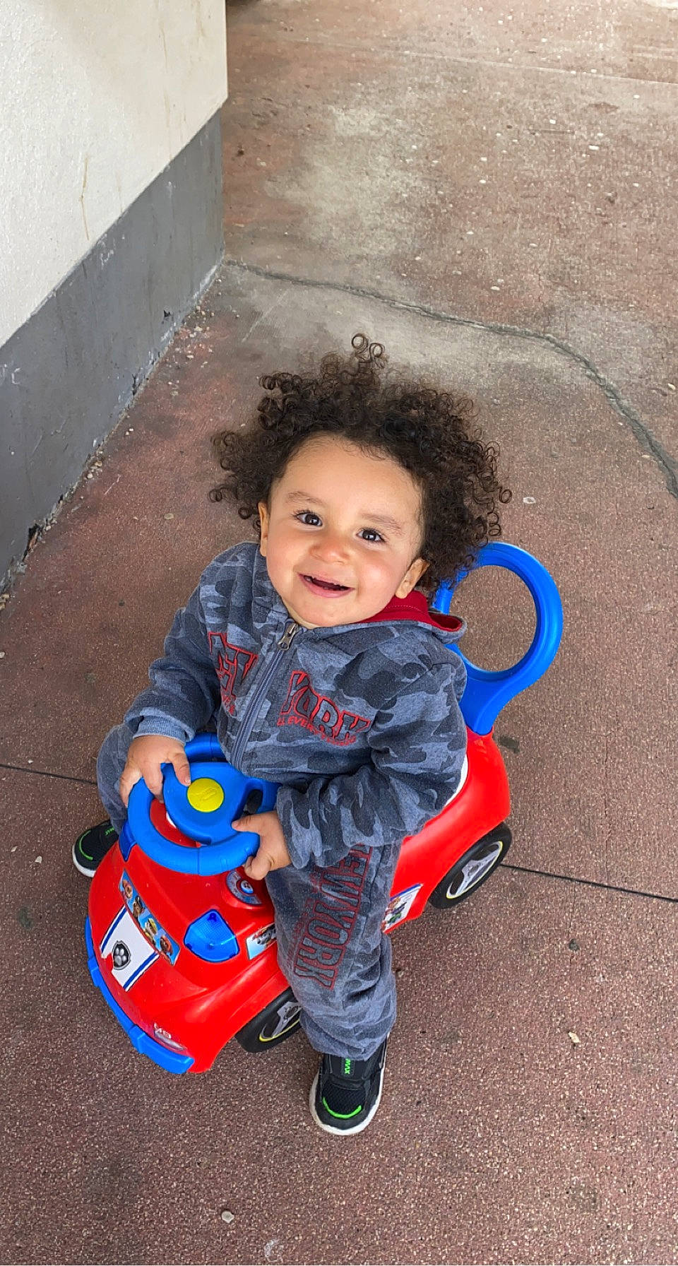 Mylow participe au concours pour gagner de l'argent avec cette photo : asphalt, baby, baby_toddler_clothing, child, clothing, concrete, electric_blue, facial_expression, flooring, fun, happy, head, joy, leisure, person, play, red, road_surface, shoe, sitting