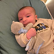 Noé participe au concours pour gagner de l'argent avec cette photo : baby, plush_toy, cushion, infant, clothing, face, hand, bedroom, soft_toy, cute, child, lying_down, indoors, smiling, portrait, comfort, warm, sleeve, fabric, young