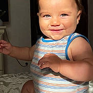 Ilyès participe au concours pour gagner de l'argent avec cette photo : baby, child, smiling, striped_clothing, onesie, indoor, bedspread, cheeks, arms, legs, skin, face, eyes, hair, light, shadow, portrait, cute, happy, infant