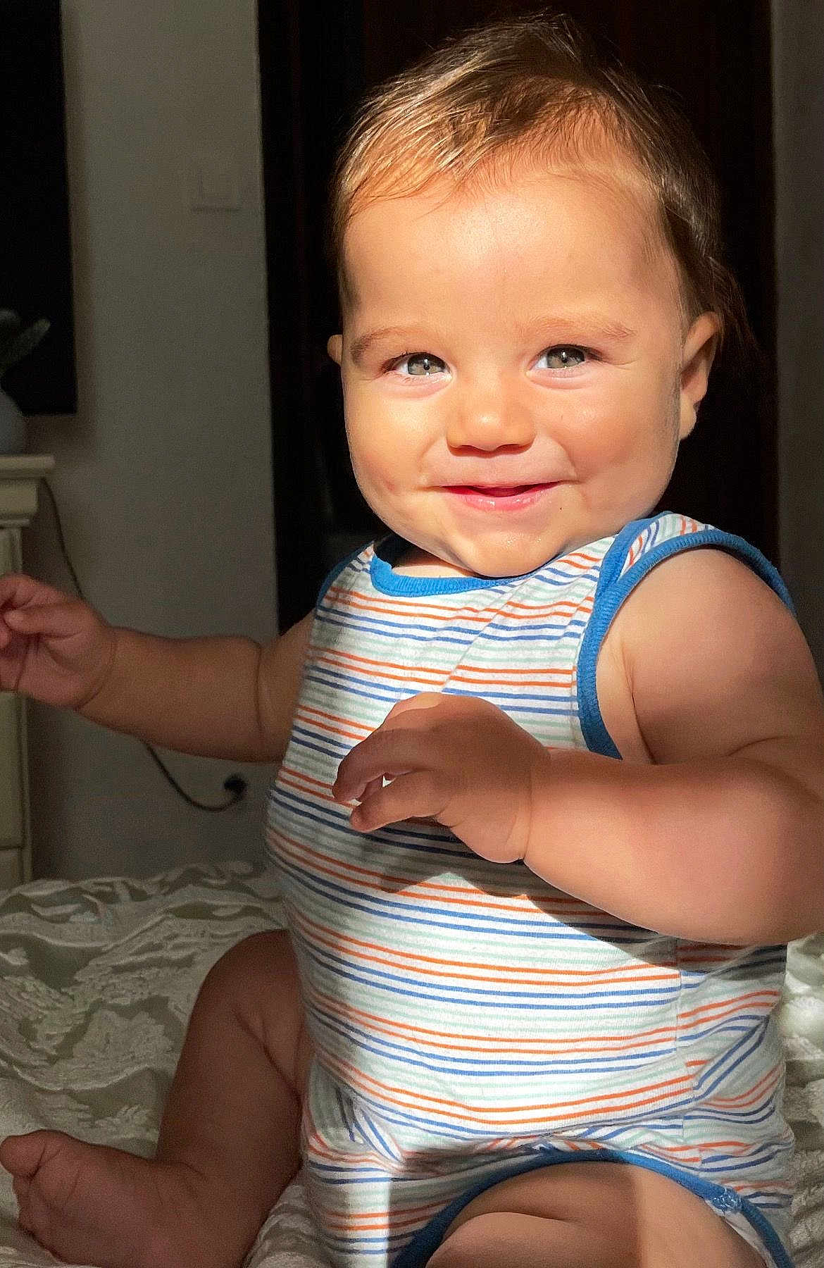 Ilyès participe au concours pour gagner de l'argent avec cette photo : baby, child, smiling, striped_clothing, onesie, indoor, bedspread, cheeks, arms, legs, skin, face, eyes, hair, light, shadow, portrait, cute, happy, infant
