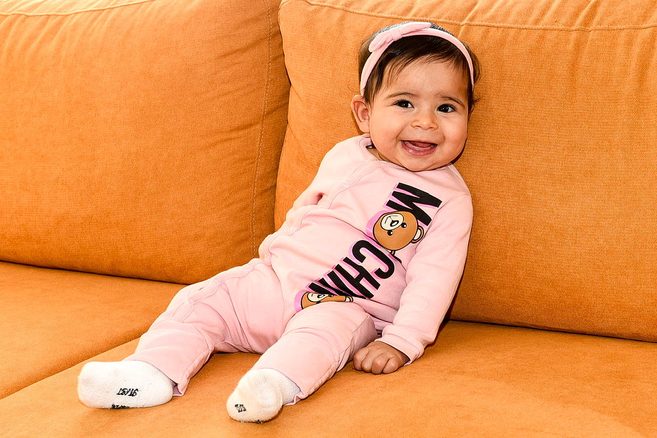 Célina a rejoint le concours — aidez-le/la à gagner de superbes lots ! arm, baby, baby_toddler_clothing, cheek, chin, comfort, couch, face, finger, floor, flooring, happy, head, joy, leg, orange, person, skin, sleeve, smile