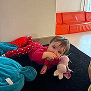 Lya a rejoint le concours — aidez-le/la à gagner de superbes lots ! baby, child, infant, toddler, plush_toy, soft_toy, carpet, indoors, playroom, crawling, lying_down, red_clothing, polka_dots, orange_sofa, smiling, hand_to_mouth, hair, face, floor, blanket