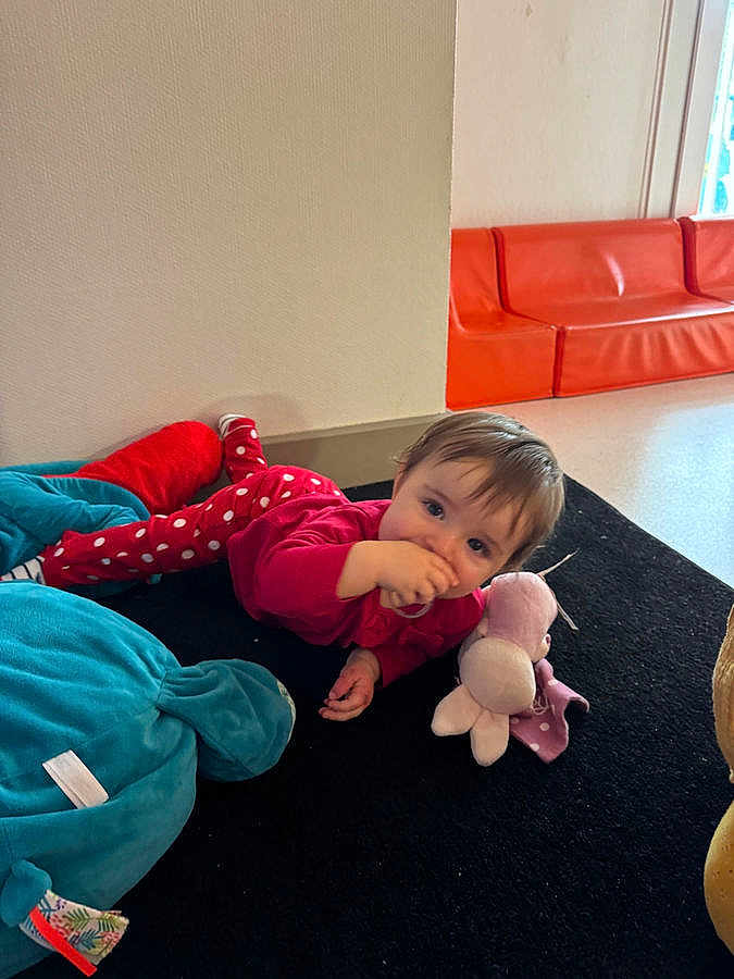 Lya a rejoint le concours — aidez-le/la à gagner de superbes lots ! baby, child, infant, toddler, plush_toy, soft_toy, carpet, indoors, playroom, crawling, lying_down, red_clothing, polka_dots, orange_sofa, smiling, hand_to_mouth, hair, face, floor, blanket