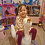 child, girl, pigtails, rocking_toy, swan, playroom, toy, castle, bookshelf, shoes, floor, wooden_floor, purple, pink, toy_horse, furniture, smile, indoor, clothing, play